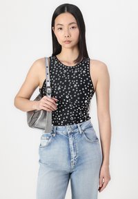 Black sleeveless top with silver stud embellishments, paired with light blue high-waisted jeans and a small silver handbag.
