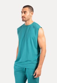 Ärmelloses, türkisfarbenes Sportoberteil aus glattem Stoff, mit Rundhalsausschnitt und lockerer Passform, kombiniert mit passenden Sporthosen.