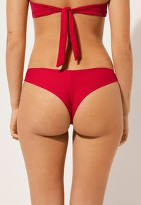 Ensemble de bikini rouge comprenant un haut à nouer dans le dos et un bas à couverture minimale. Tissu lisse et design épuré avec une couleur vive.