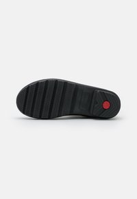 Semelle de chaussure noire en caoutchouc avec une texture antidérapante. Présente des rainures horizontales et un accent circulaire rouge près du talon. Design léger et durable.