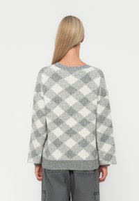 Grauer und weißer übergroßer Pullover mit einem Rautenmuster, rundem Halsausschnitt und gerippten Bündchen. Weiche Textur und entspannte Passform.