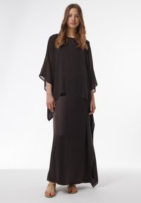 Schwarzes, fließendes zweiteiliges Outfit mit einem locker sitzenden Oberteil mit weiten Ärmeln und einem langen, schmalen Rock. Glattes, leichtes Material.