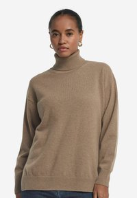 Beige Rollkragenpullover aus weichem Strickmaterial, mit lockerer Passform, gerippten Bündchen und Saum. Die Textur wirkt warm und gemütlich.