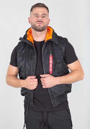 Black padded vest with an orange lining, zip closure, and front pockets. Features a red tag on the zipper, crafted from lightweight material.
