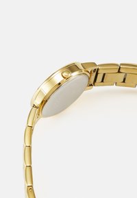 Gold-tone wristwatch featuring a round case, flat silver dial, and a textured metal bracelet with linked segments. Button on the side.
