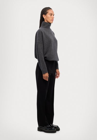 Pull en maille gris à col roulé avec épaules tombantes, associé à un pantalon noir taille haute et des chaussures noires à semelles épaisses. Style simple et décontracté.