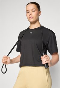 Must musta sportlik särk lühikeste varrukatega, millel on diskreetne logo ja millega koos on must hüppenöör, mida hoitakse õlavarre kõrgusel.