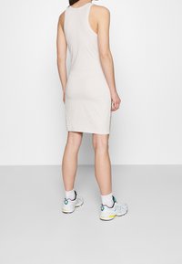 Svetle béžové tankové šaty vyrobené z měkké tkaniny, ke kolenům, s přiléhavým střihem. Nosené s bílými a tyrkysovými teniskami.