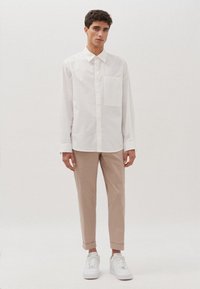 Witte overhemd met knoopsluiting en een borstzak, gecombineerd met beige broeken met opgerolde manchetten en witte sneakers. Glad materiaal, casual pasvorm.