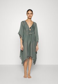 Pareo in morbido e leggero tessuto verde, con scollatura a V e chiusura con lacci, arricchito da frange decorative lungo l'orlo e le maniche.