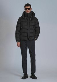 Black puffer jacket with a high collar and shiny accents, paired with dark tailored pants and black shoes. Smooth texture, casual design.