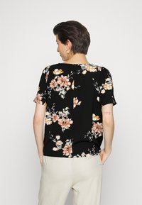 Top preto de mangas curtas com um padrão floral em pêssego e branco. Ajuste solto com hemline reta; o tecido parece macio e leve.
