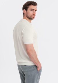 Camisa polo de punto de manga corta en color blanco roto, con un tejido texturizado, cuello y puños acanalados, combinada con pantalones gris con rayas.