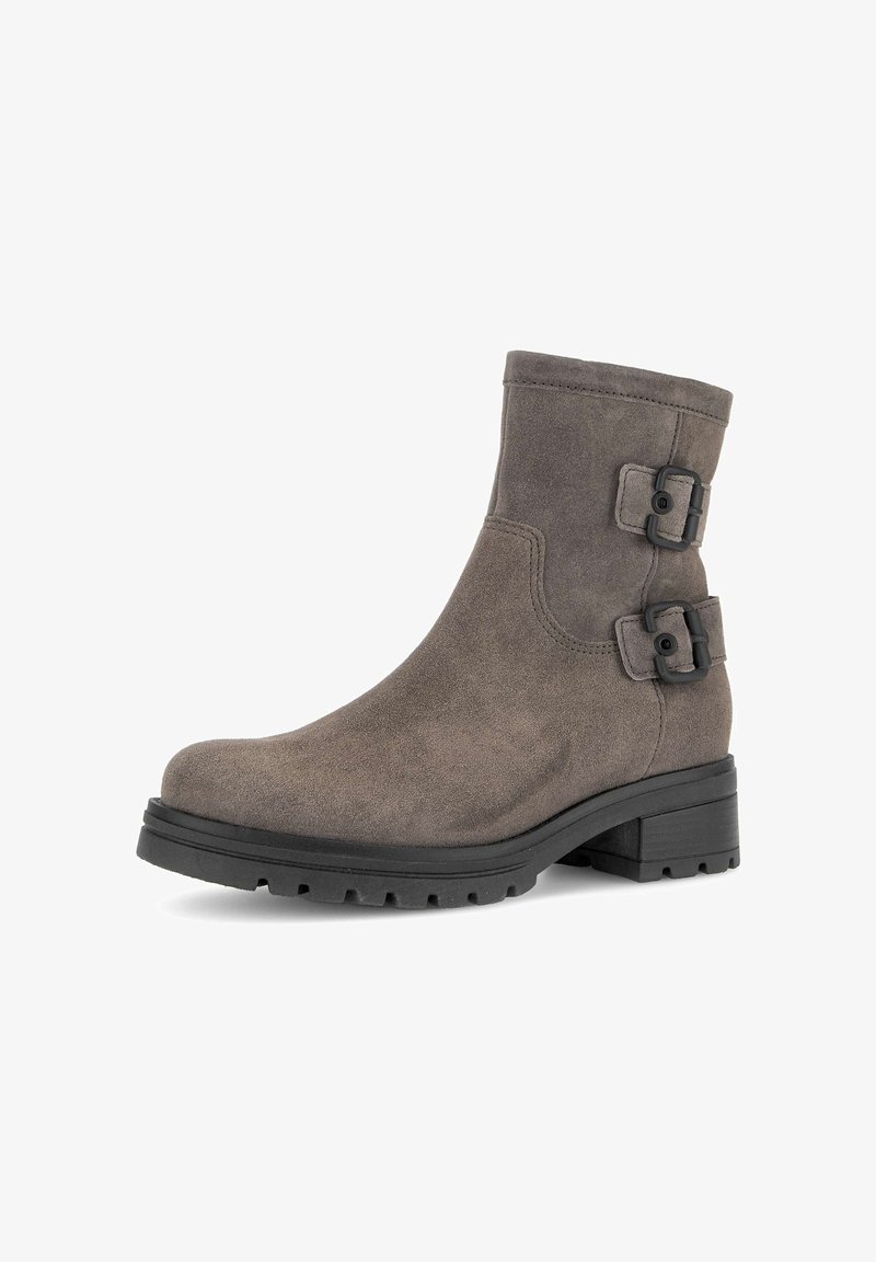 Bottine en suede marron avec deux accents de boucle noire, bout rond et semelle en caoutchouc texturé. Elle possède un petit talon bloc et des détails cousus.
