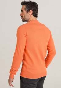 Oranger Strickpullover mit langen Ärmeln, Rundhalsausschnitt, gerippten Bündchen und Saum. Glatte Textur mit tailliertem Design.