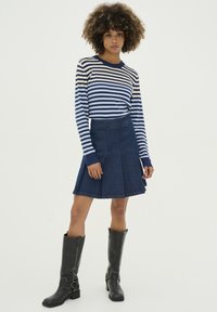 Pruhovaný top s dlhým rukávom v tmavomodrej a bielej farbe, džínsová áčková sukňa, čierne čižmy po kolená s prackovými detailmi a štruktúrovaným materiálom.