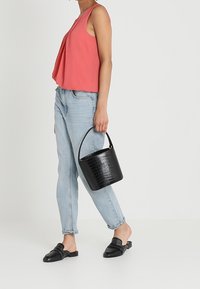 Borsa a secchiello nera con stamping in coccodrillo, top senza maniche color corallo, jeans azzurri chiari e mules neri con borchie e apertura sul retro.