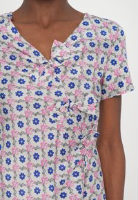 Kvetinové šaty s šedobielym vzorom a modrými a ružovými kvetmi. Majú zvratový detail na výstrihu a krátke rukávy.