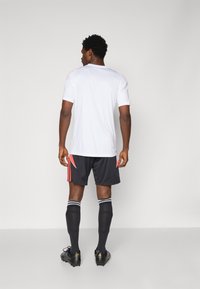 Hvid kortærmet tr�æningsskjorte med røde accenter, parret med sorte shorts med røde striber og sorte sportssokker, båret med sorte fodboldstøvler.