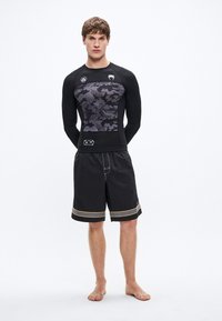 Czarna koszulka z długim rękawem i wzorem szarego kamuflażu, połączona z czarnymi szortami z żółtym wykończeniem na brzegu.