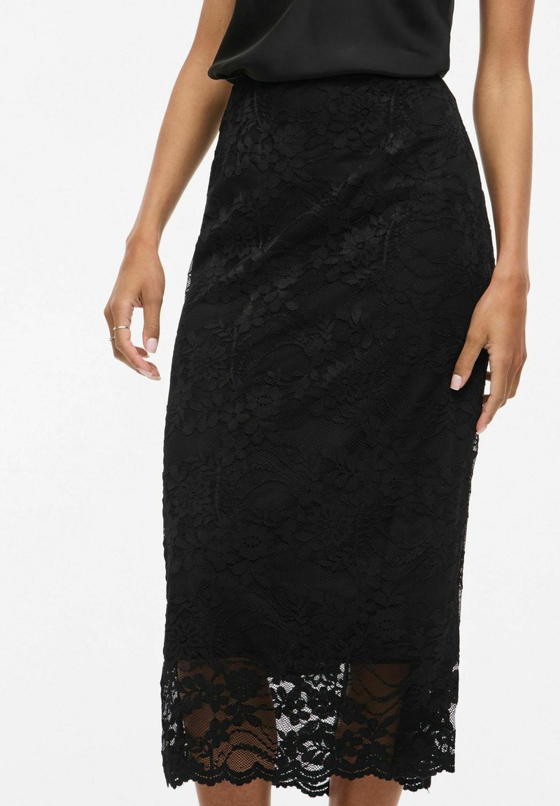 Jupe midi en dentelle noire avec un motif floral, un tissu texturé et un ourlet festonné. Silhouette ajustée avec une légère brillance.