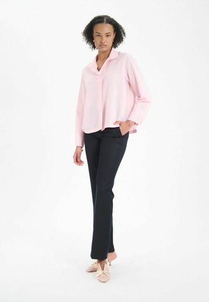 Chemise à boutons rose clair à manches longues, associée à un pantalon marine foncé. La chemise présente une coupe décontractée et une texture subtile.
