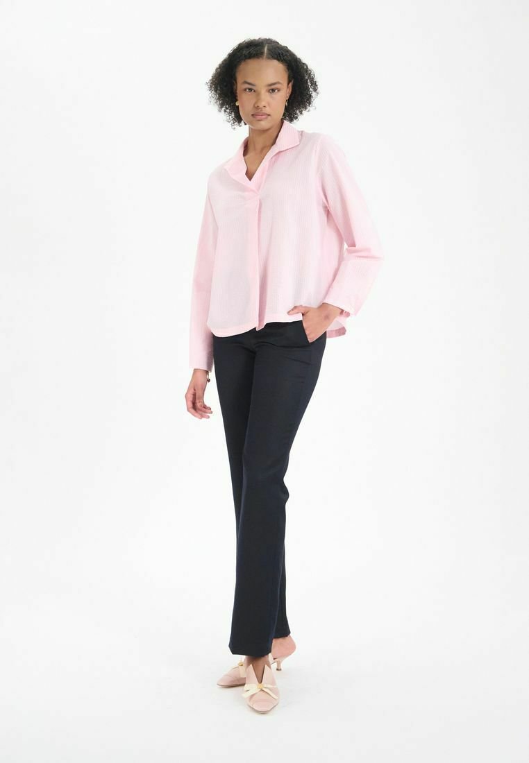Chemise à boutons rose clair à manches longues, associée à un pantalon marine foncé. La chemise présente une coupe décontractée et une texture subtile.