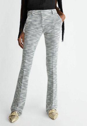 Woman wearing high-waist black and white checkered pants with side pockets, black top, and metallic gold pointed shoes.