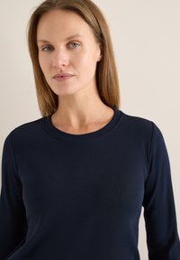 Haut à manches longues bleu marine en tissu côtelé avec un col rond et une silhouette ajustée. Texture lisse avec un minimum de détails.