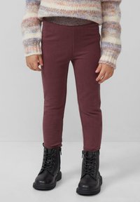Bordeaux leggings met een zachte afwerking, gecombineerd met zwarte veterschoenen. De trui heeft meerkleurige strepen en een grof gebreide textuur.