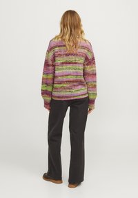 Maglione lavorato a maglia multicolore con righe orizzontali in rosa, verde e viola, caratterizzato da maniche lunghe e una vestibilità ampia. Abbinato a pantaloni neri.
