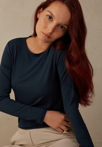 Marineblaue Langarmbluse aus glattem Stoff, mit rundem Ausschnitt und körpernahem Schnitt, kombiniert mit beigen Hosen.