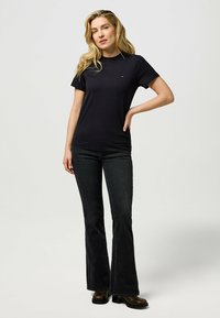 Sorte kortærmede t-shirt med rund hals og et lille logo på brystet, parret med flagrende mørke jeans og ankelstøvler.