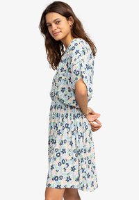 Bloemendress met een ontspannen pasvorm, korte mouwen en een gathered taille. De stof is licht met pasteltinten en marineblauwe bloemenpatronen.
