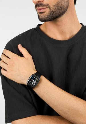 Mann trägt schwarzes T-Shirt und schwarzen Smartwatch am linken Handgelenk, auf dem Zeit und Gesundheitsdaten angezeigt werden, Hand ruht auf rechter Schulter.
