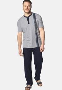 Gray cotton short-sleeve shirt with navy trim, button placket, and vertical stripe featuring text. Paired with navy pants and brown sandals.