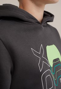 Grijze hoodie met een trekkoord, voorzien van een groen en blauw grafisch ontwerp met witte contouren. Zachte stof met een gestructureerd oppervlak.