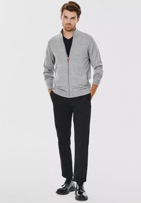 Szara kardigan zapinana na zamek, wykonana z miękkiego materiału, z prążkowanym kołnierzem i mankietami, w zestawieniu z czarnymi spodniami slim-fit i czarnymi butami.