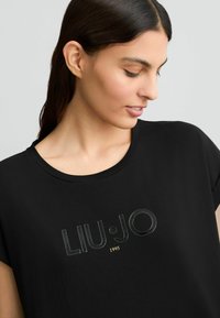 T-shirt nera a maniche corte realizzata in morbido cotone, con un logo lucido "LIU•JO 1995" sul davanti e scollatura rotonda.