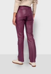 Los pantalones de cuero morado presentan un corte ajustado y un diseño de pierna recta con bolsillos traseros. Combinados con zapatos de color claro.