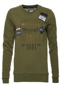 Sudadera verde oliva de mangas largas, cuello redondo y varios parches. Presenta letras metálicas y adornos como detalles de marca.