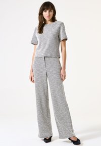 Conjunto de dos piezas en un patrón de espiga en blanco y negro. Top de manga corta y pantalones de pierna ancha con un acabado texturizado. Acentos en el hombro.
