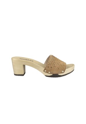 Beige heeled sandal with wooden sole, wide suede strap adorned with gold studs, and black rubber grip on underside.