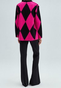 Schwarz-rosa Pullover mit Diamantmuster, langen Ärmeln, lockerer Passform und rundem Ausschnitt, kombiniert mit schwarzen ausgestellten Hosen.