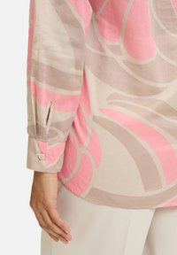 Leichte, gemusterte Bluse mit abstraktem pinken und beigen Design, Knopfmanschetten und seitlichen Schlitzdetails. Glatte Textur.