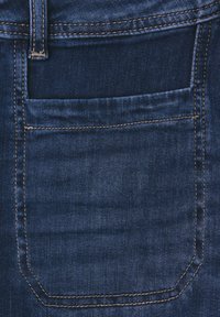 Mörkblå denimjeans har en bakficka med synlig sömnad och en böjd form, som visar en slät yta och subtila slitage-mönster.