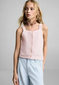 Svetlo roza pletena top s kvadratnim izrezom, sprednjim gumbom in ozkimi naramnicami, v kombinaciji z ohlapnimi svetlo modrimi kavbojkami.