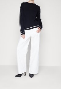 Pull noir en maille avec des rayures blanches sur les manches, associé à un pantalon large blanc et ample et des talons pointus noirs. Design simple, lignes épurées.