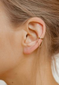 Goldene Creolen mit einer geschwungenen Form, die ein Kettenglied-Detail aufweisen. Der Ohrring ist am äußeren Rand des Ohrläppchens befestigt.