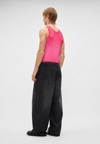 Rosa Tanktop mit breiten Schulterträgern, kombiniert mit übergroßen schwarzen Jeans aus Denim mit klassischem Fünf-Taschen-Design.